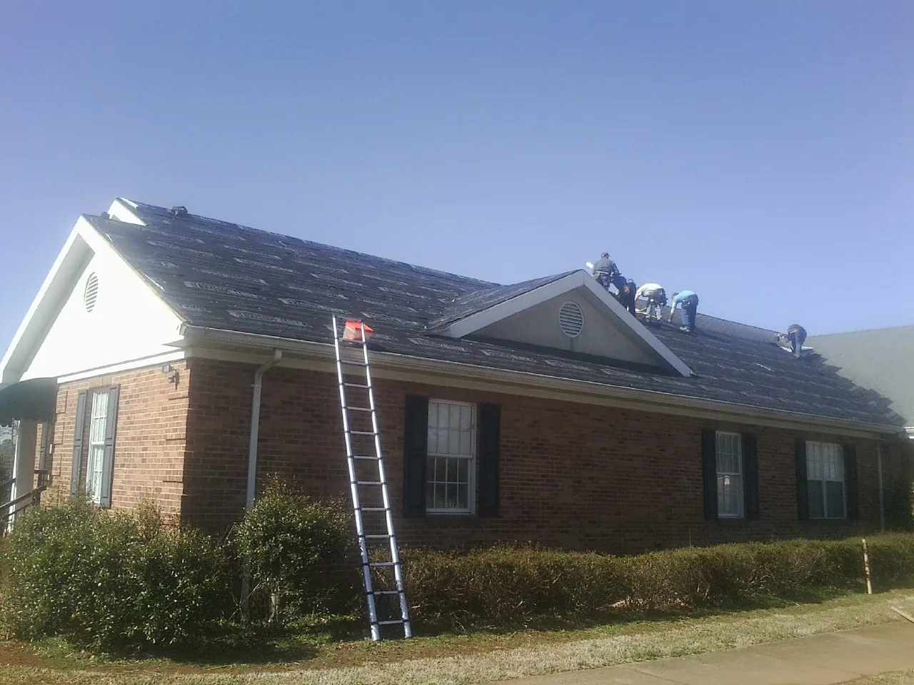 Crew tearing shingles off a brick ranch roof with a ladder set — Emergency Roof Repair work by our crew in New Braintree