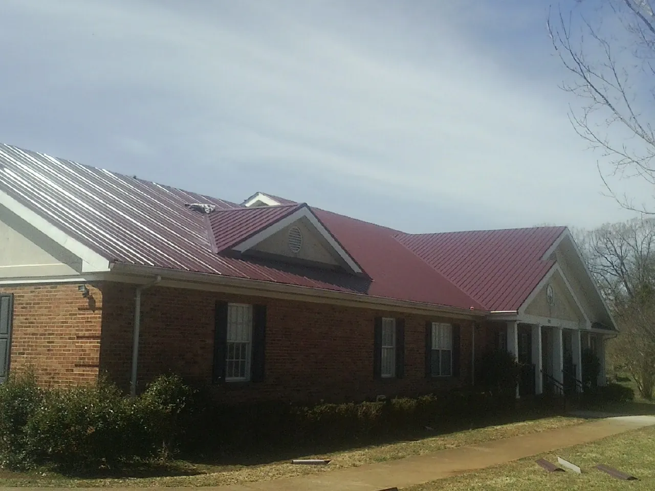 Red metal roof with gabled entries on a long brick building, from a Hail Damage Roof Repair job in New Braintree