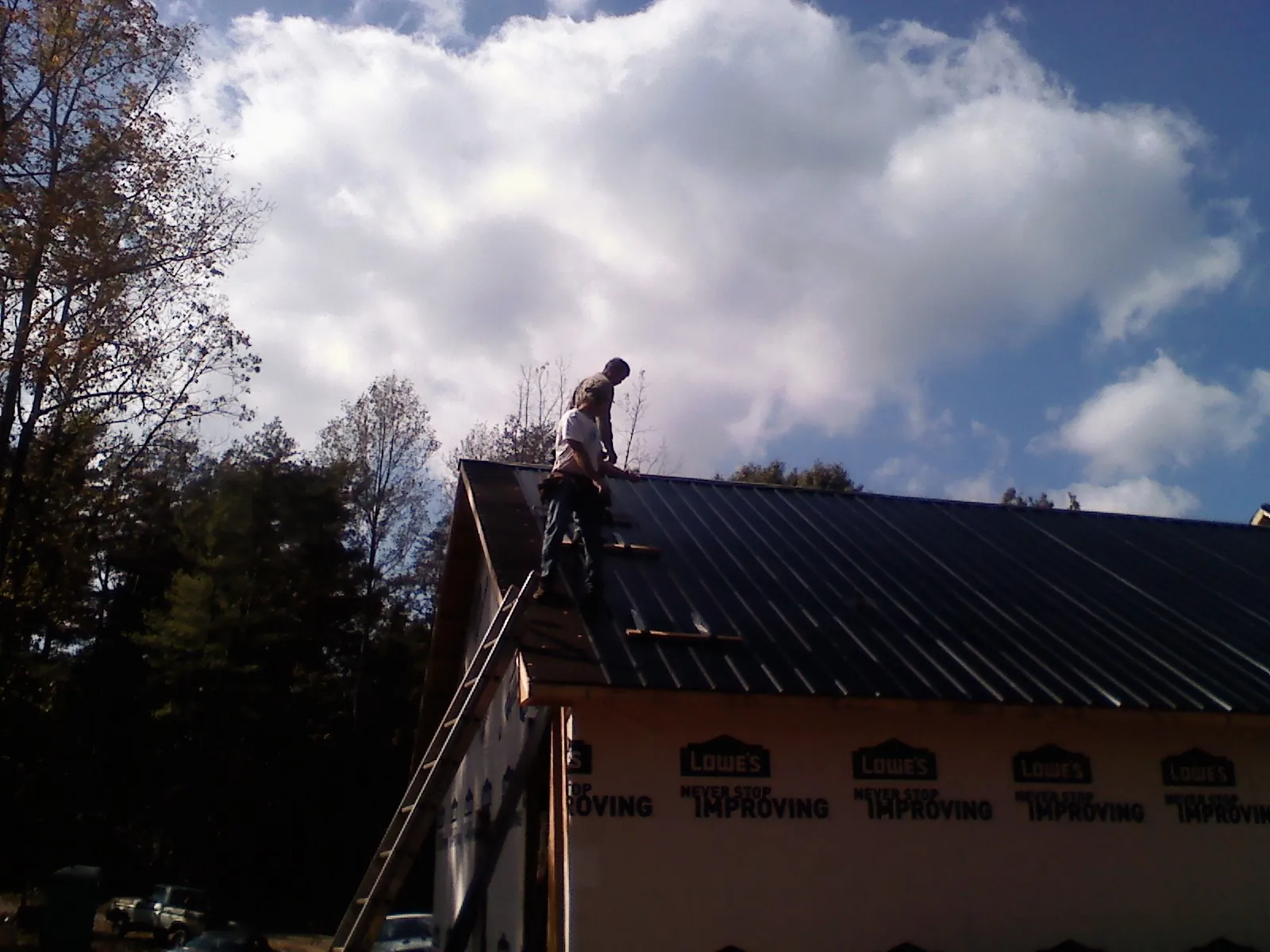 Roofer fastening dark metal panels high against a cloudy sky, from a Roof Inspection job in New Braintree