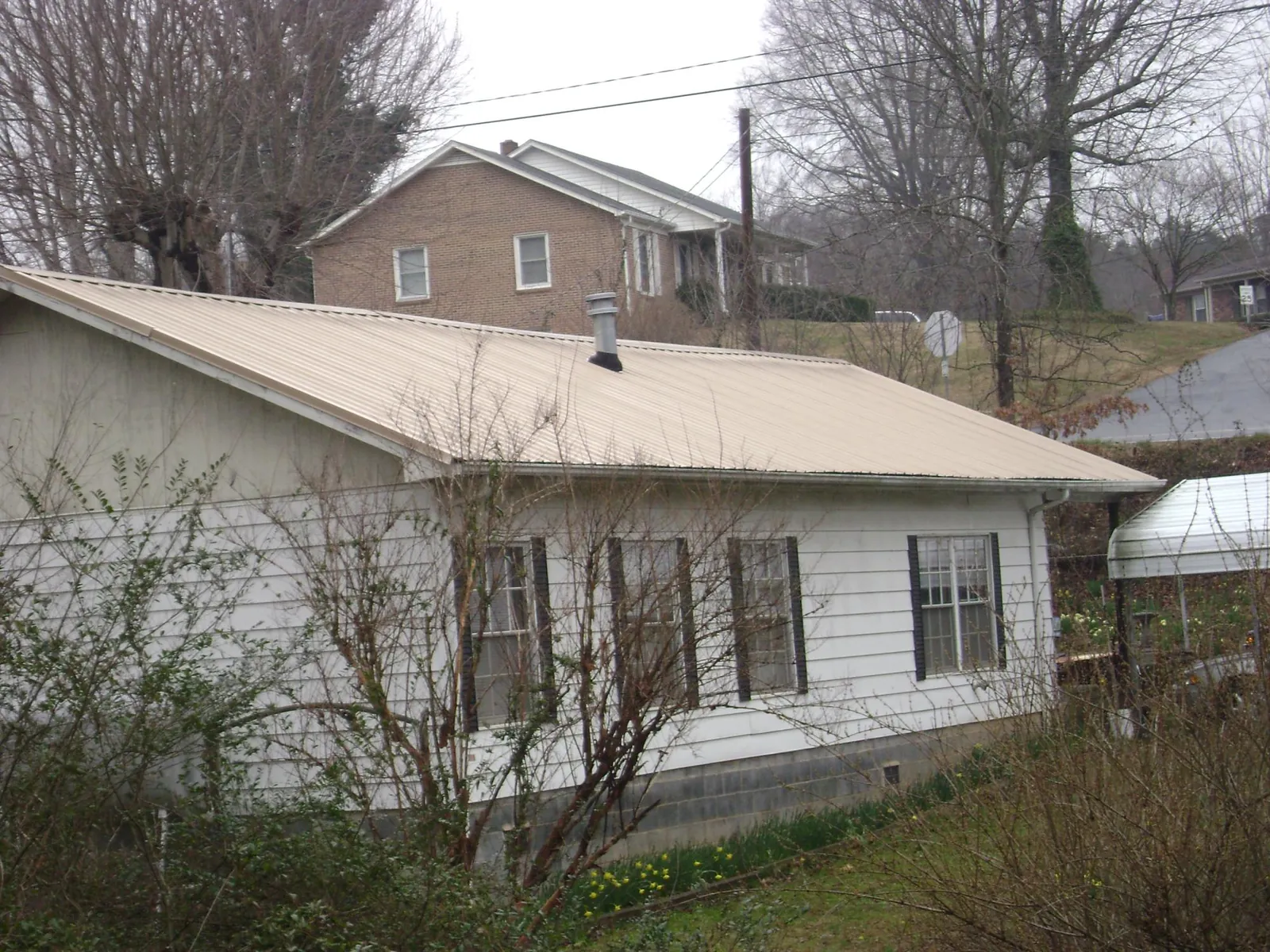 Tan metal roof on a white sided house set into a hillside — Commercial Roofing by Roofing Brothers in New Braintree