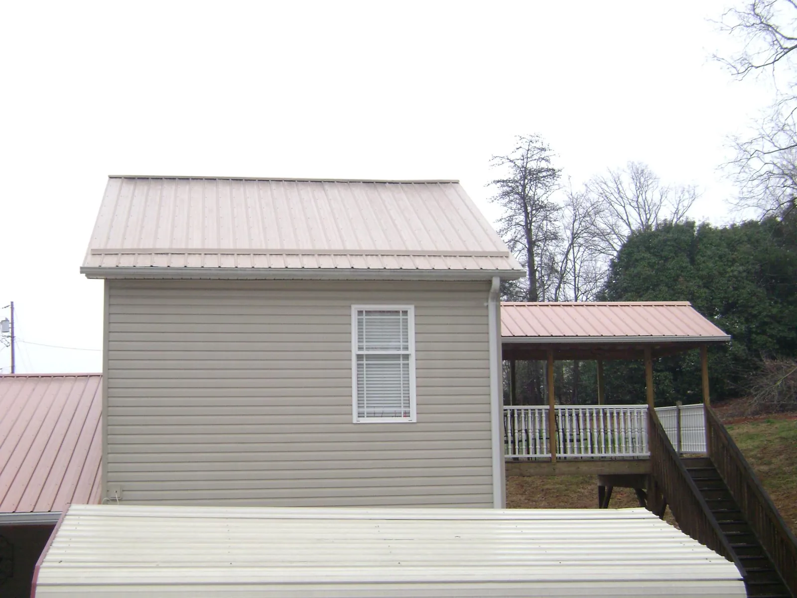 Tan metal roofs on a two story addition and attached porch, from a Roof Replacement job in New Braintree